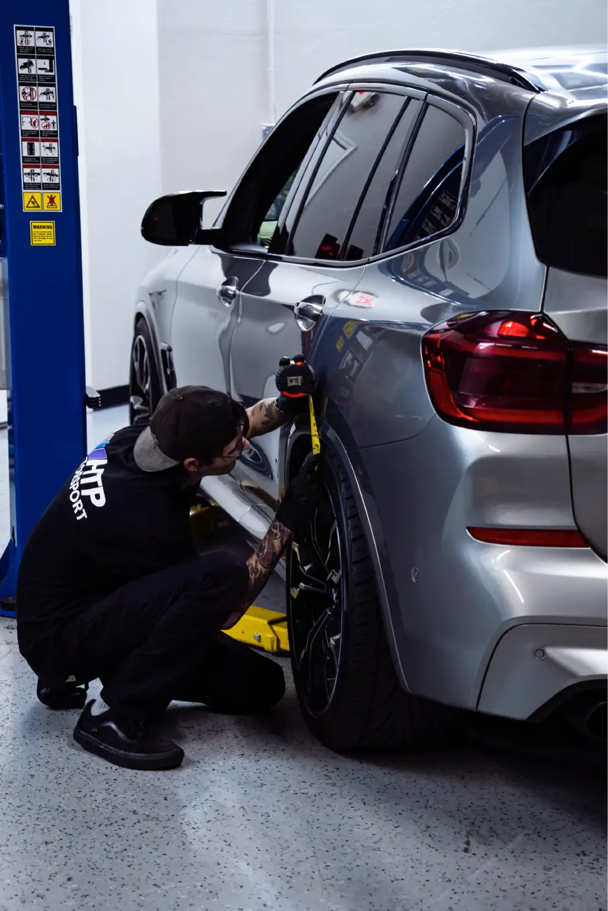 HTP Motorsport technician checking wheel alignment on a silver BMW X-model SUV on a lift