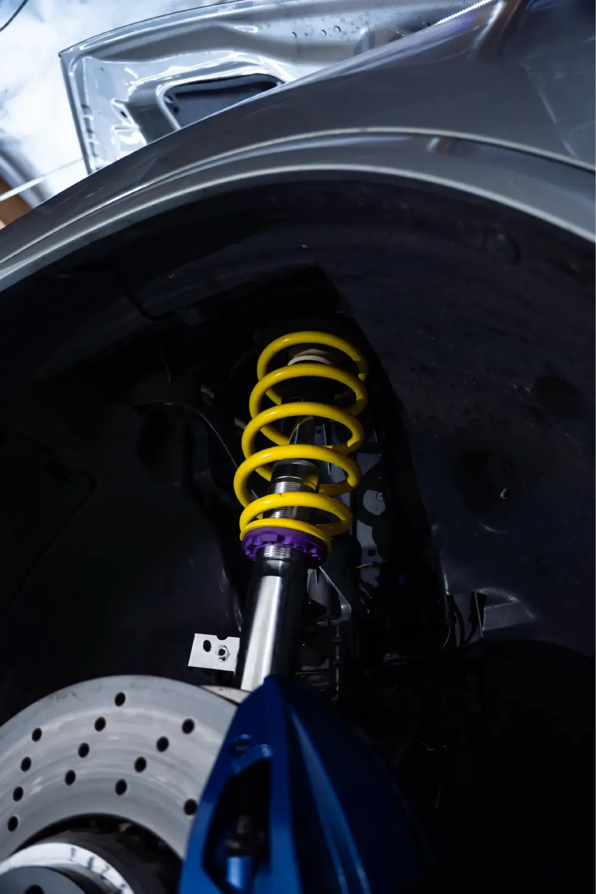 Close-up of a yellow coilover spring above a cross-drilled brake rotor in a wheel well.