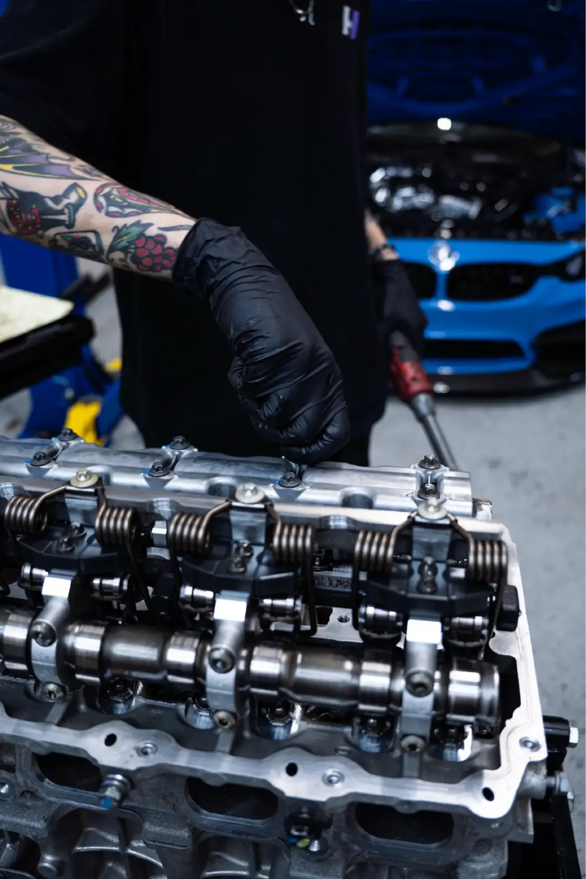 Gloved technician working on an exposed cylinder head with the camshafts and valve springs visible