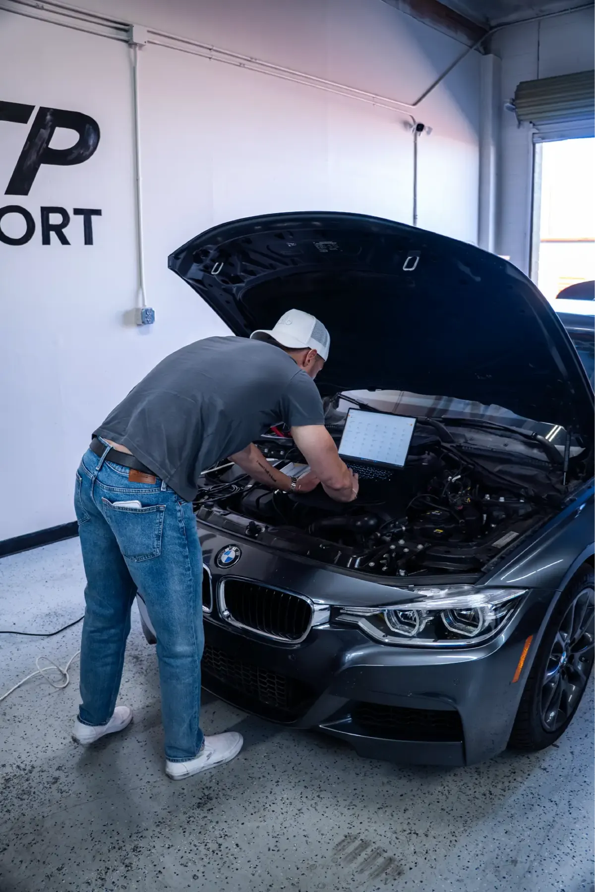 HTP Motorsport technician working under the open hood of a grey BMW 3 Series with a laptop on the engine bay.