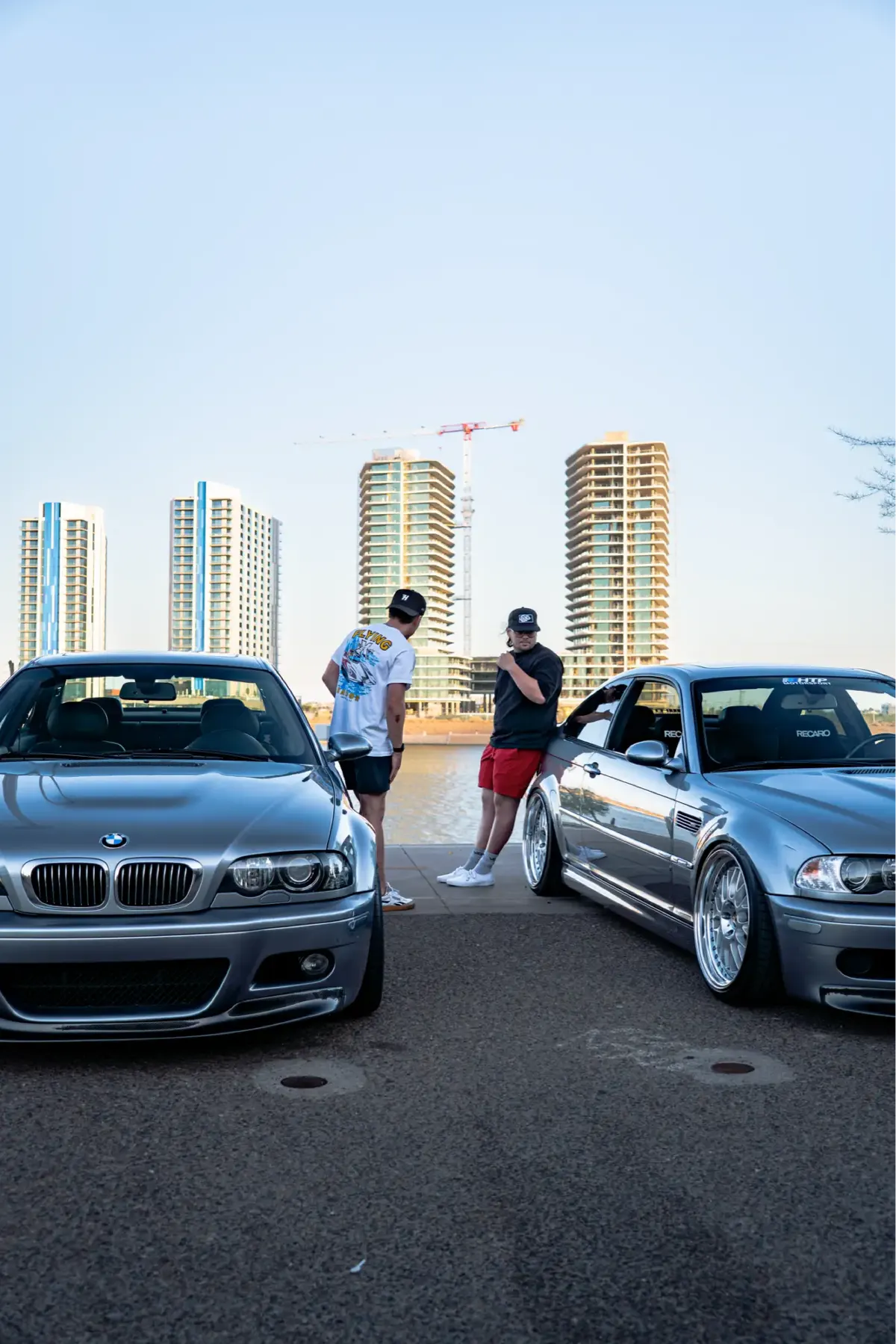 Two silver BMW M3 (E46) coupes parked facing each other by the water