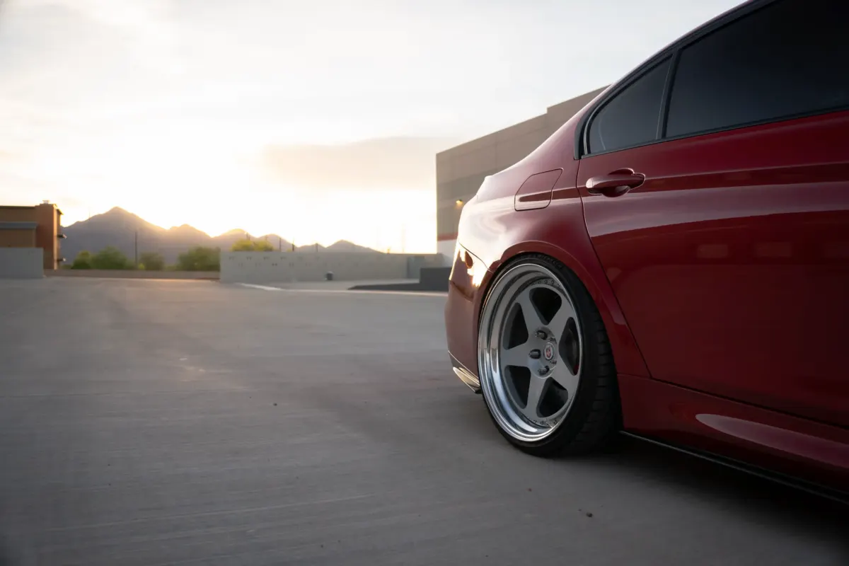 Low close-up of a maroon BMW M3 (F80) rear wheel and tire at sunset.