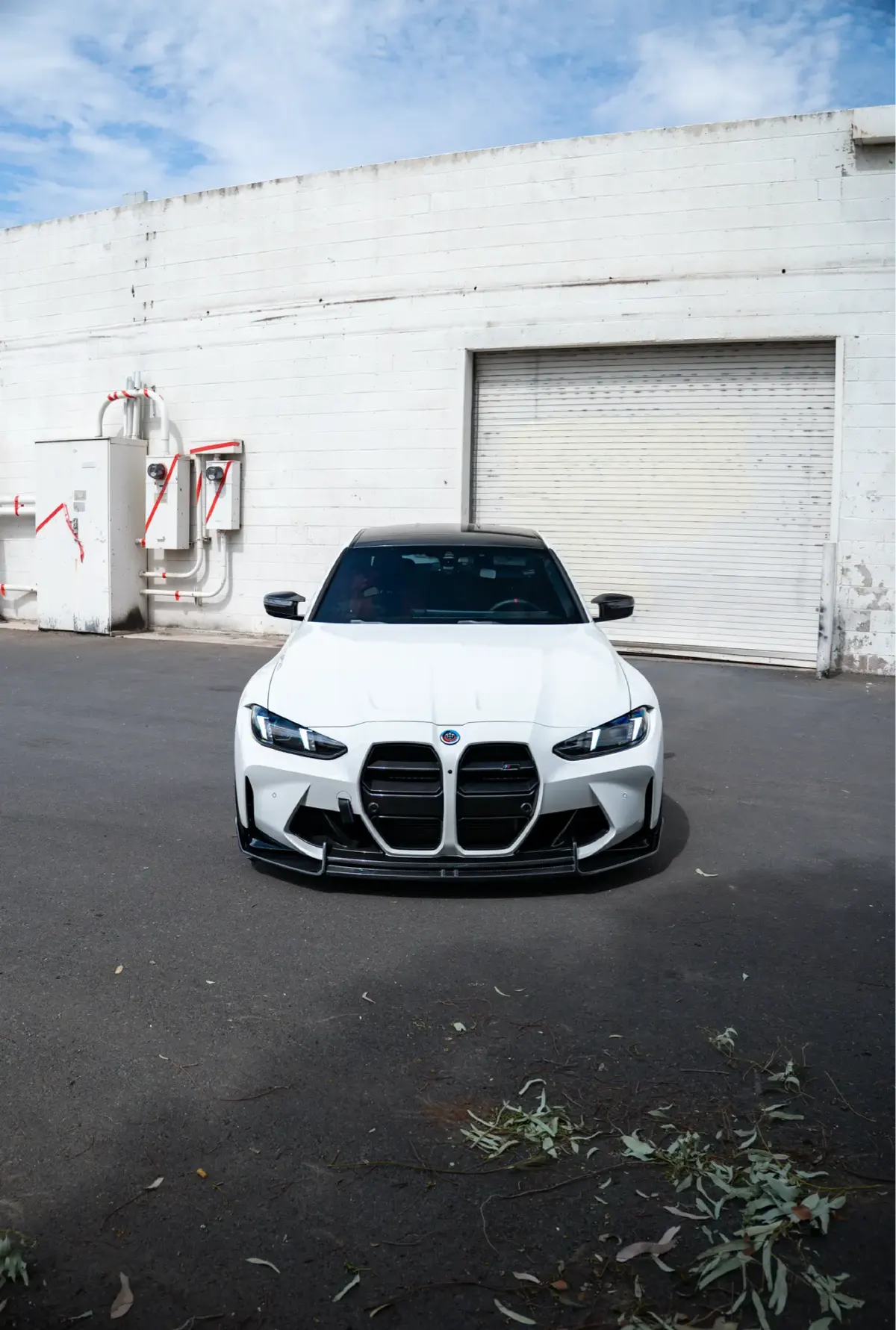 Front view of a white G80 M3 with its vertical kidney grille, parked outside a warehouse