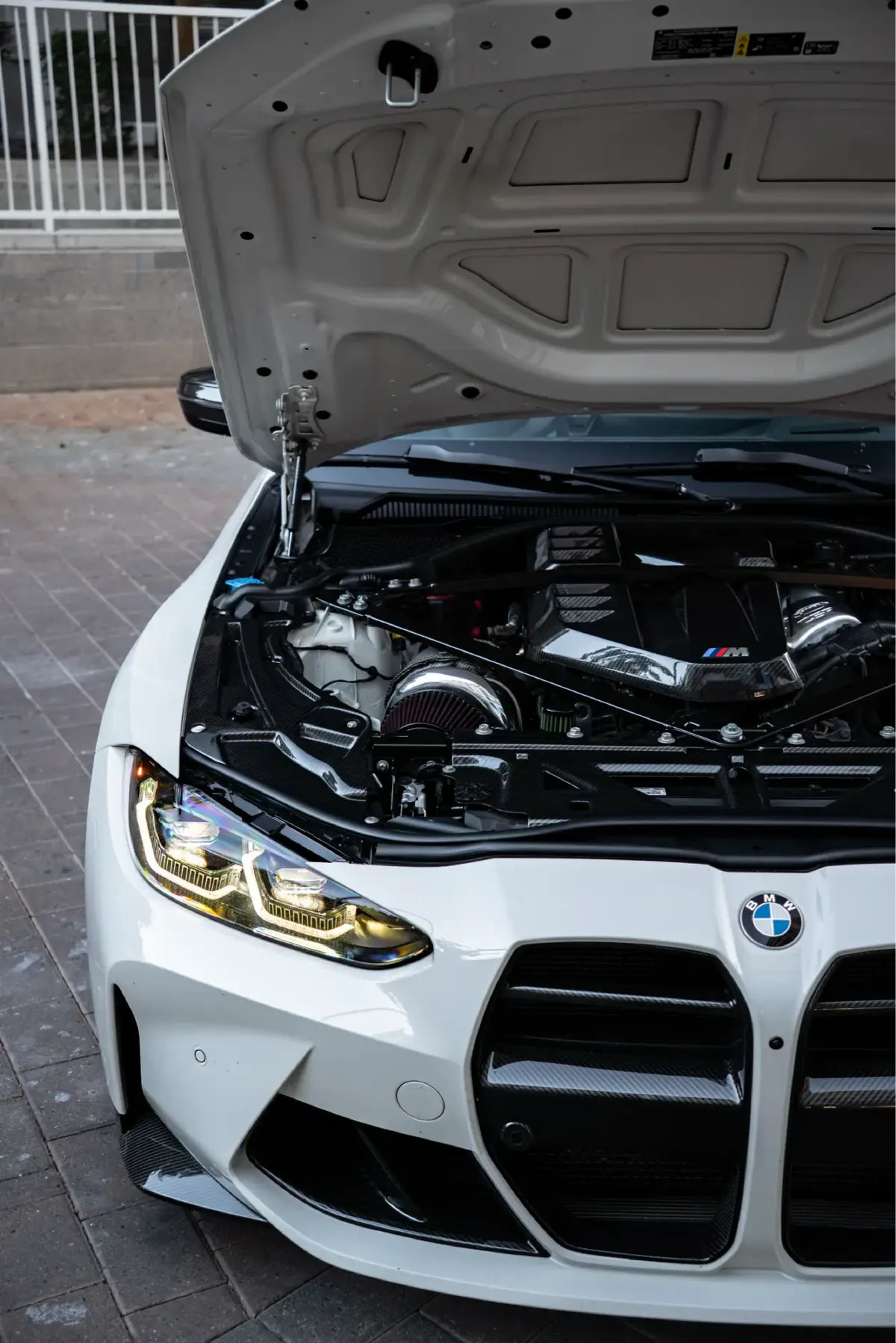 White BMW M4 (G82) with its hood open, showing the S58 twin-turbo inline-six engine bay