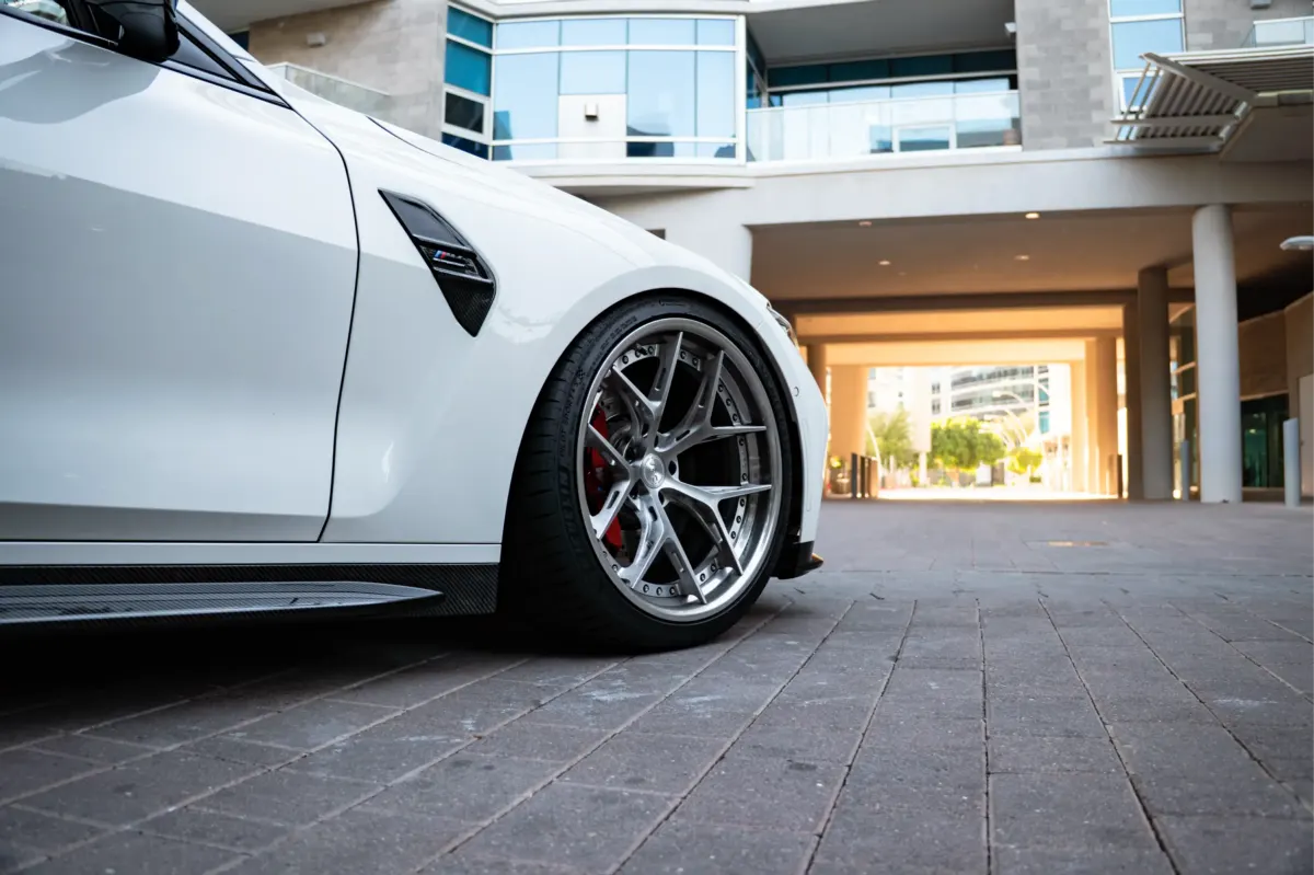 Bronze multi-spoke wheel on a white BMW M4 filling the front wheel arch, seen low from the side on a brick plaza