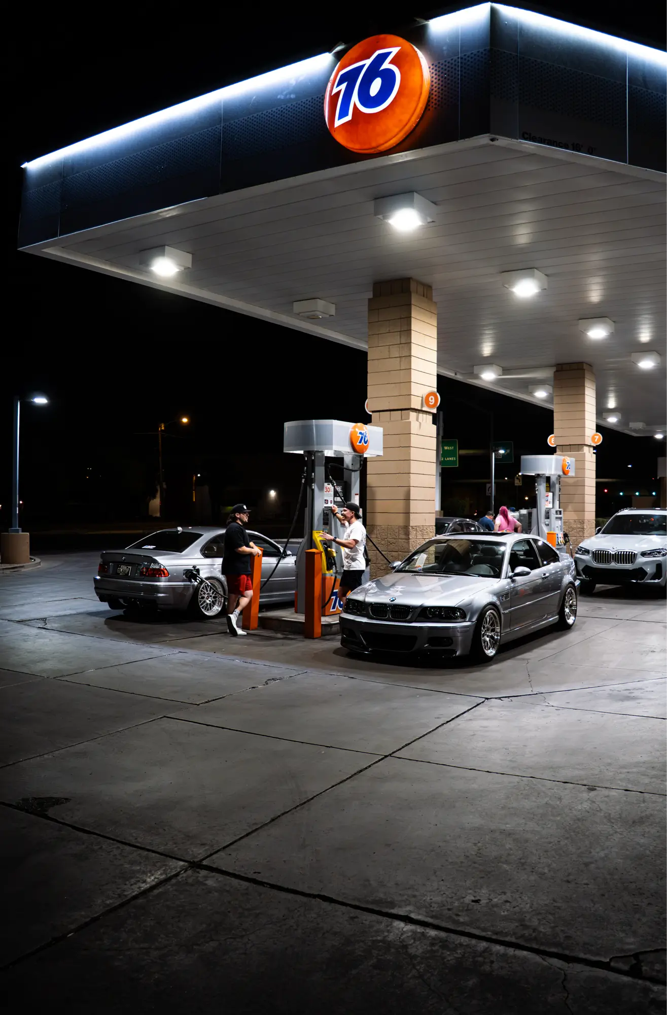 A pair of silver BMW E46 M3s parked together at a gas station at night.
