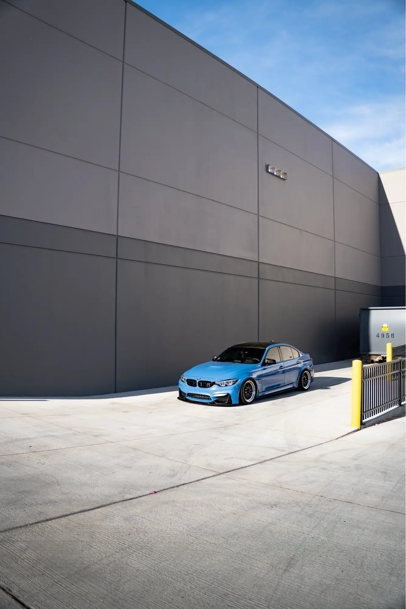 Blue BMW M3 (F80) shown front three-quarter near a loading dock.