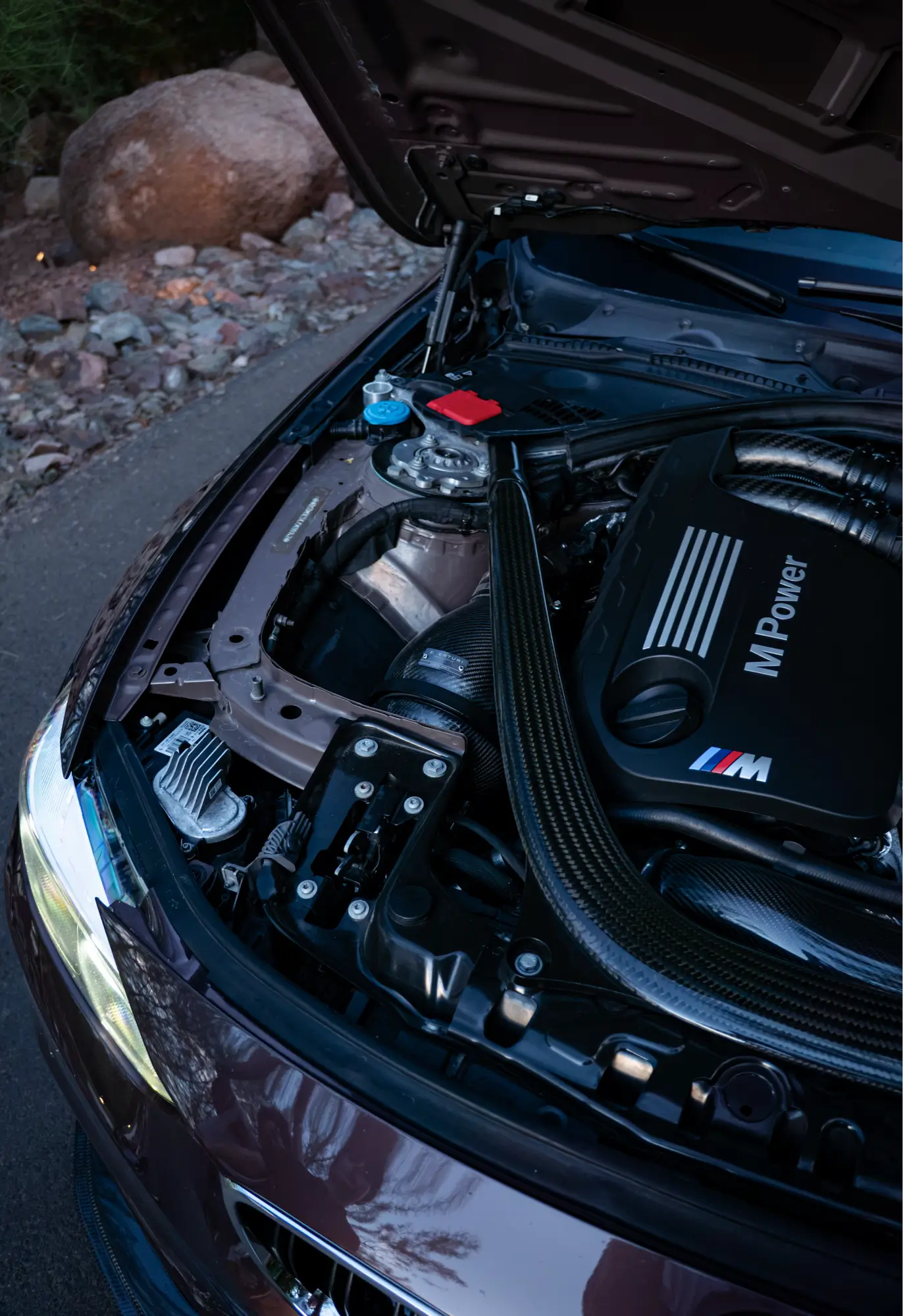 Maroon BMW M3 (F80) with its hood open, engine bay visible at dusk.