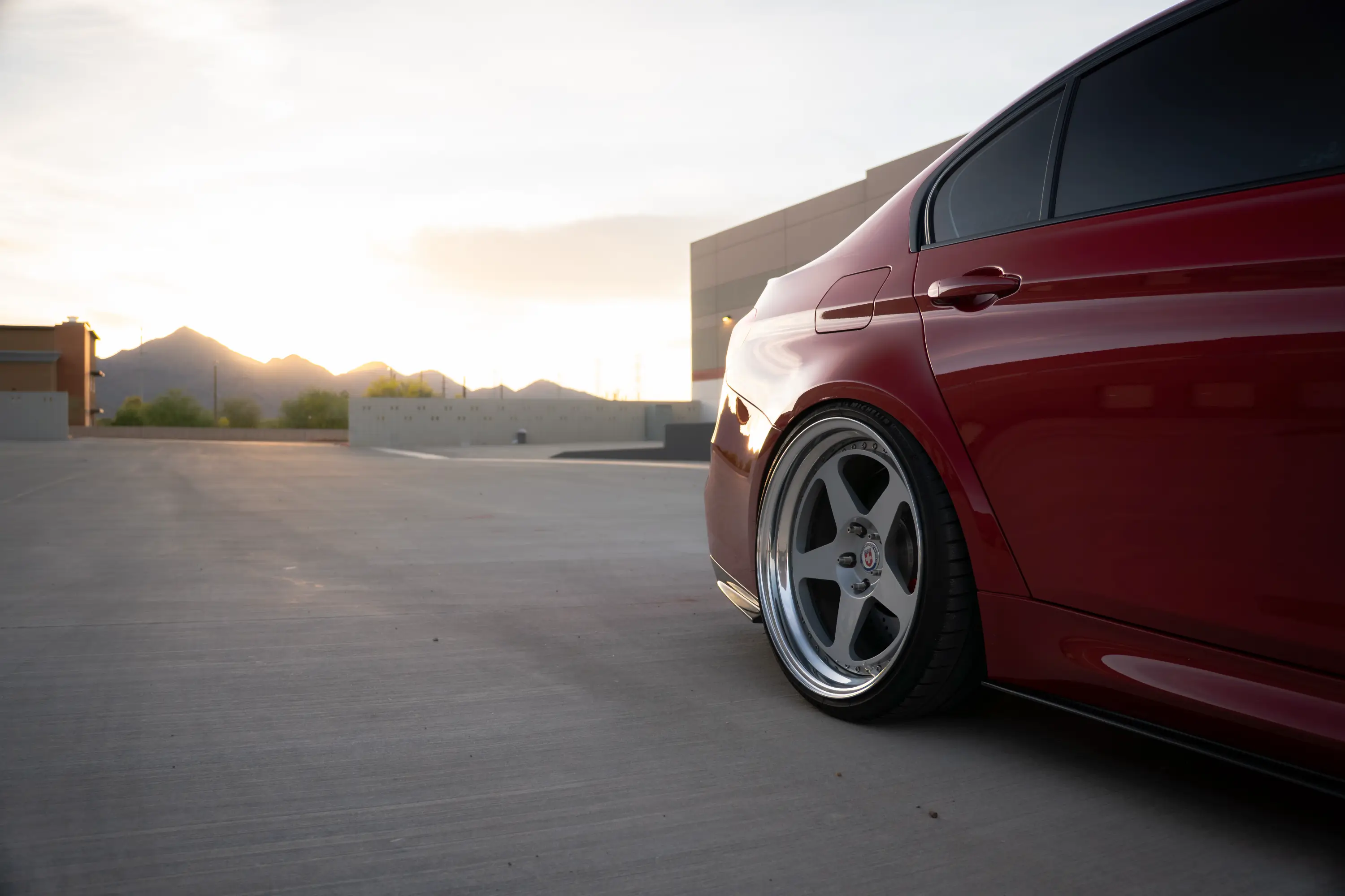 Close-up of a maroon BMW M3 (F80)'s rear wheel at sunset.