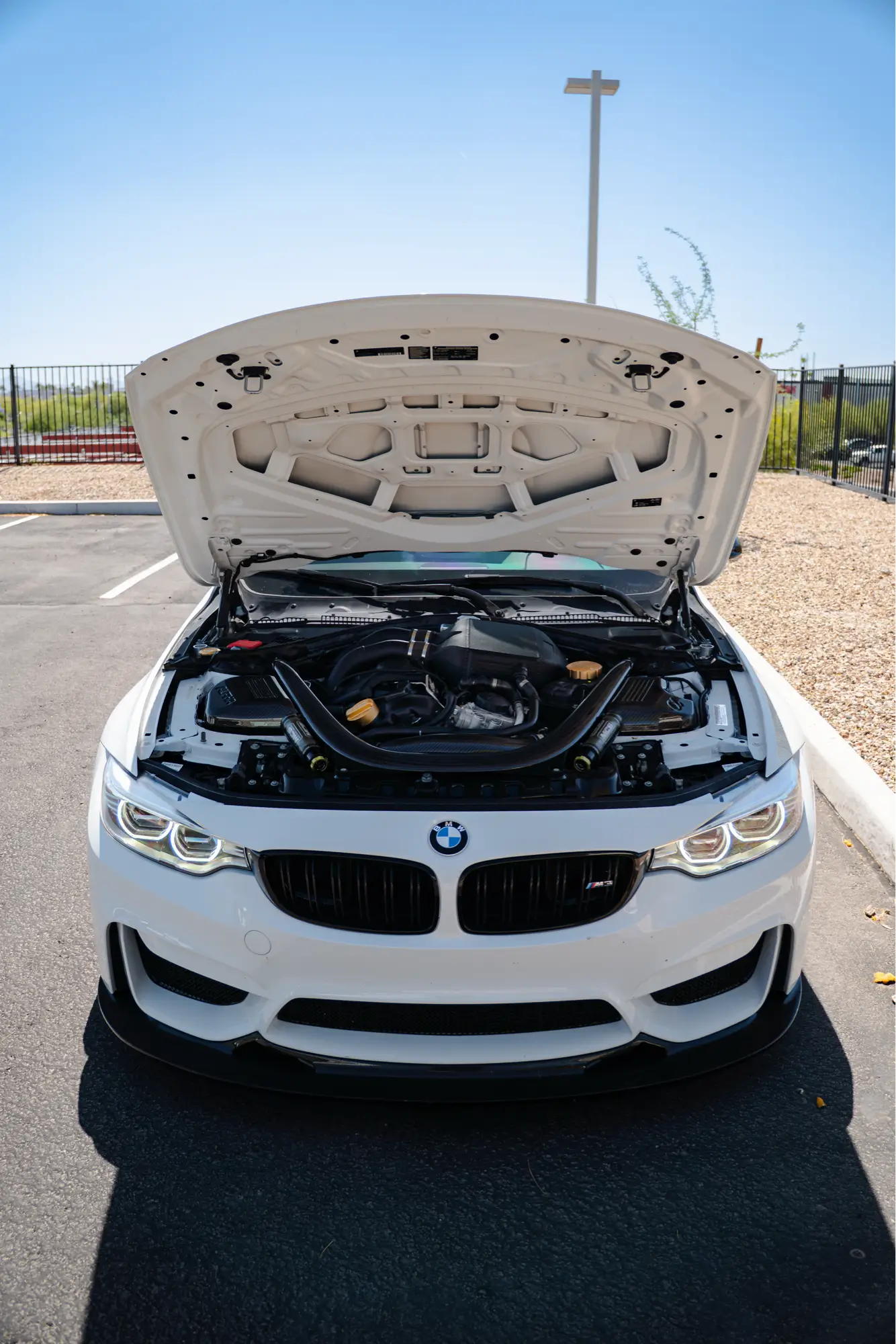 White BMW M3 (F80) with its hood open, revealing the engine bay.