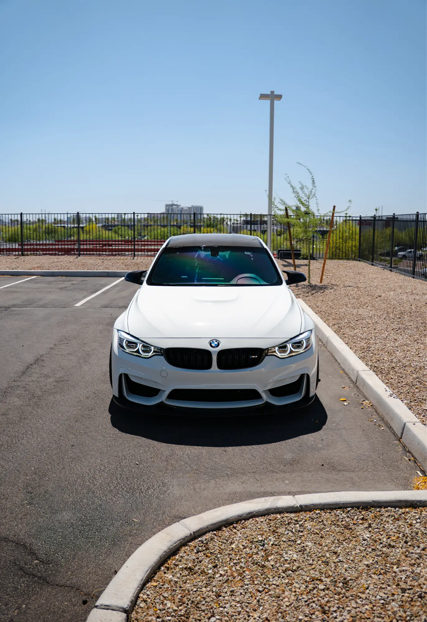 Straight-on front view of a white BMW M3 (F80) in a parking lot.