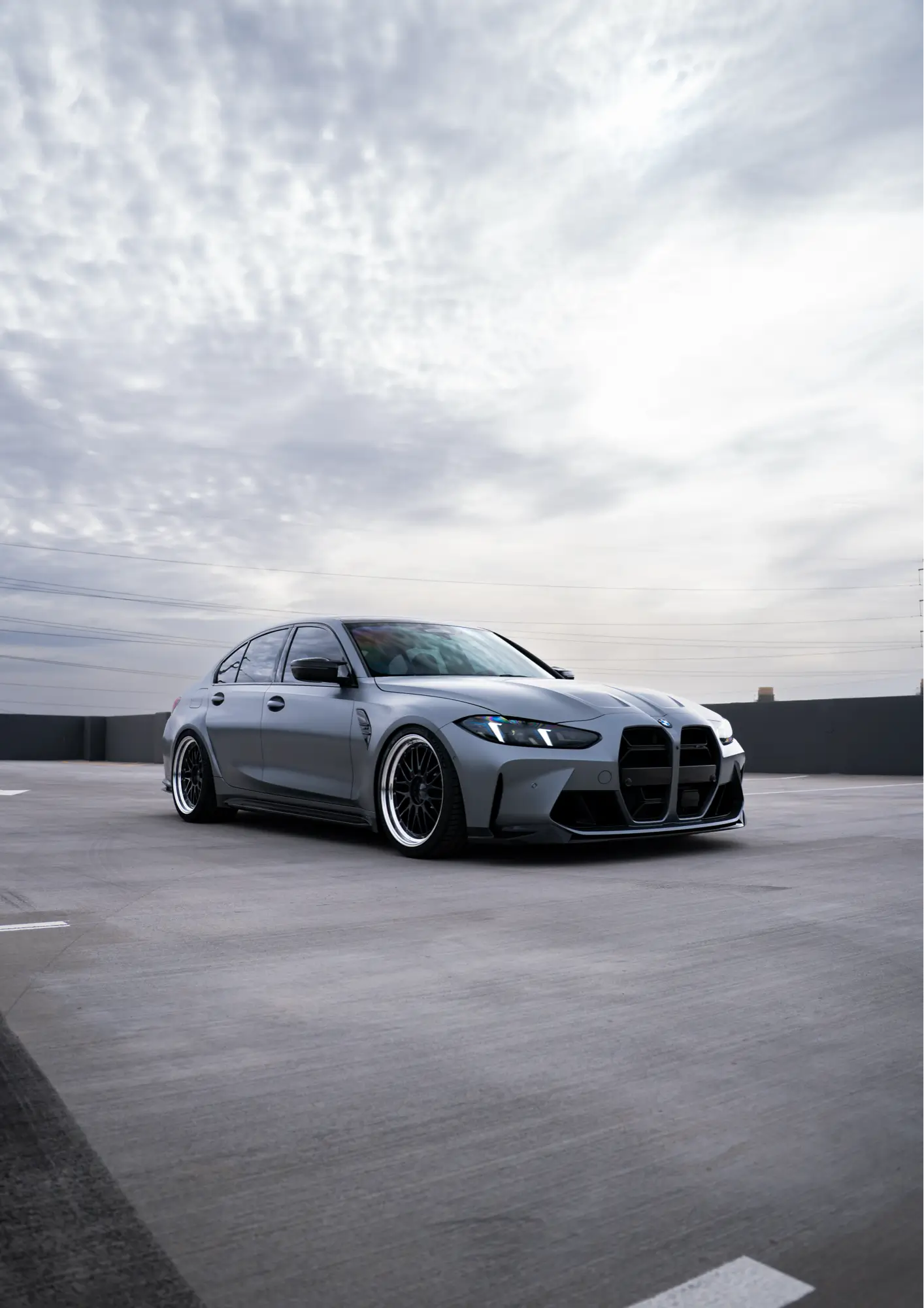 Grey BMW M3 (G80) shown front three-quarter on a rooftop lot.