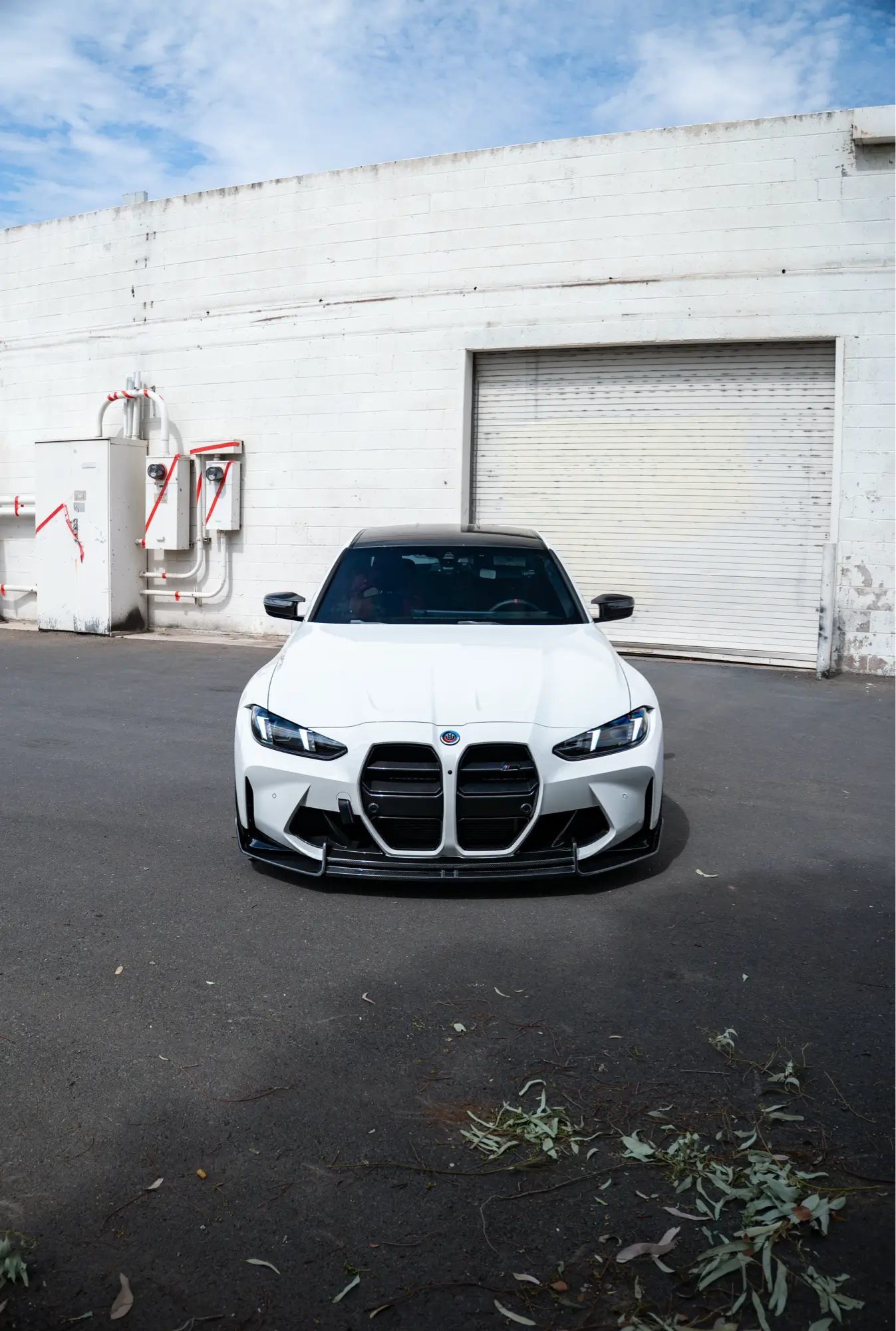 Straight-on front view of a white BMW M3 (G80) inside a warehouse.