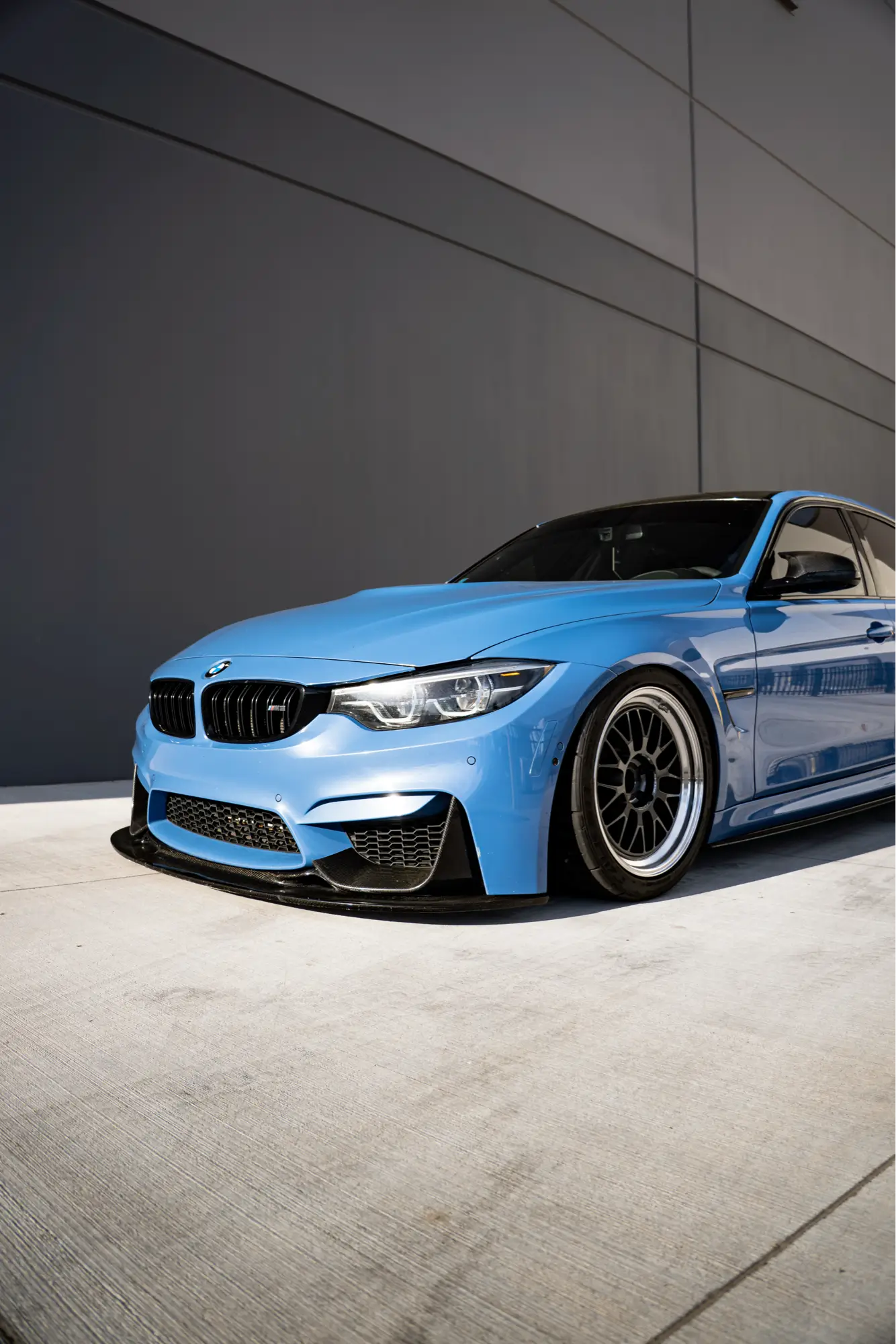 Blue BMW M3/M4 (F80/F82) with a carbon fiber roof, shown front three-quarter.
