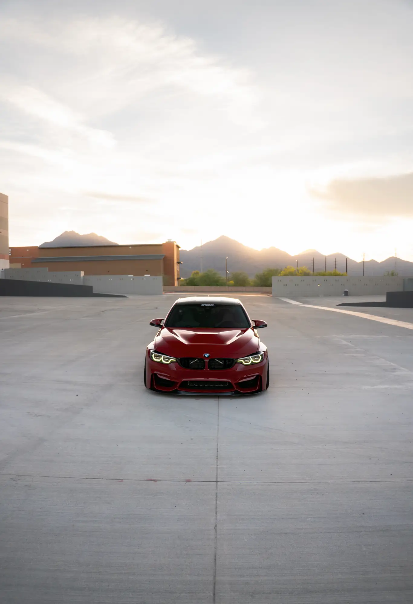 Straight-on front view of a red BMW M3/M4 (F8x) with mountains in the background.