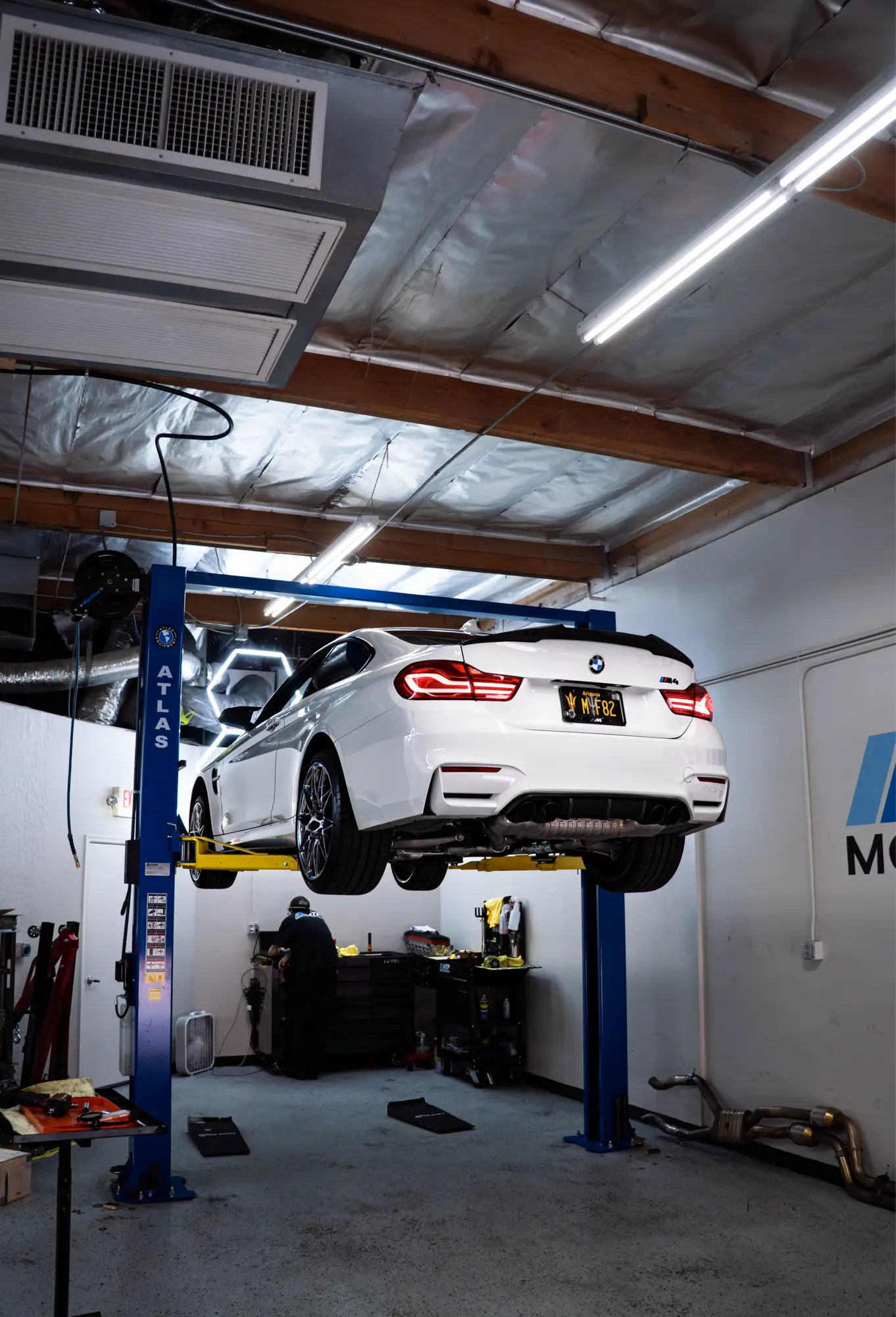 White BMW M4 (F82) raised on a lift at the HTP Motorsport shop.