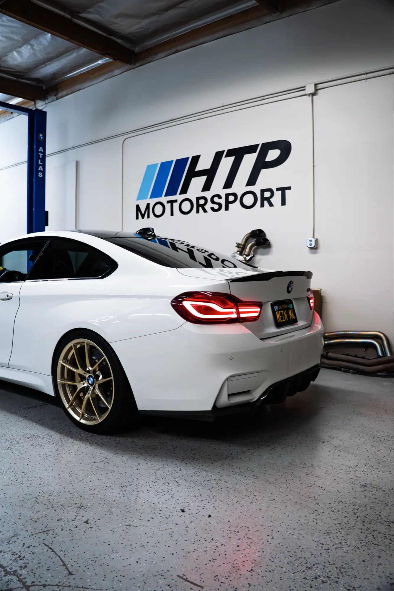 White BMW M4 (F82) shown rear three-quarter at the HTP Motorsport shop.