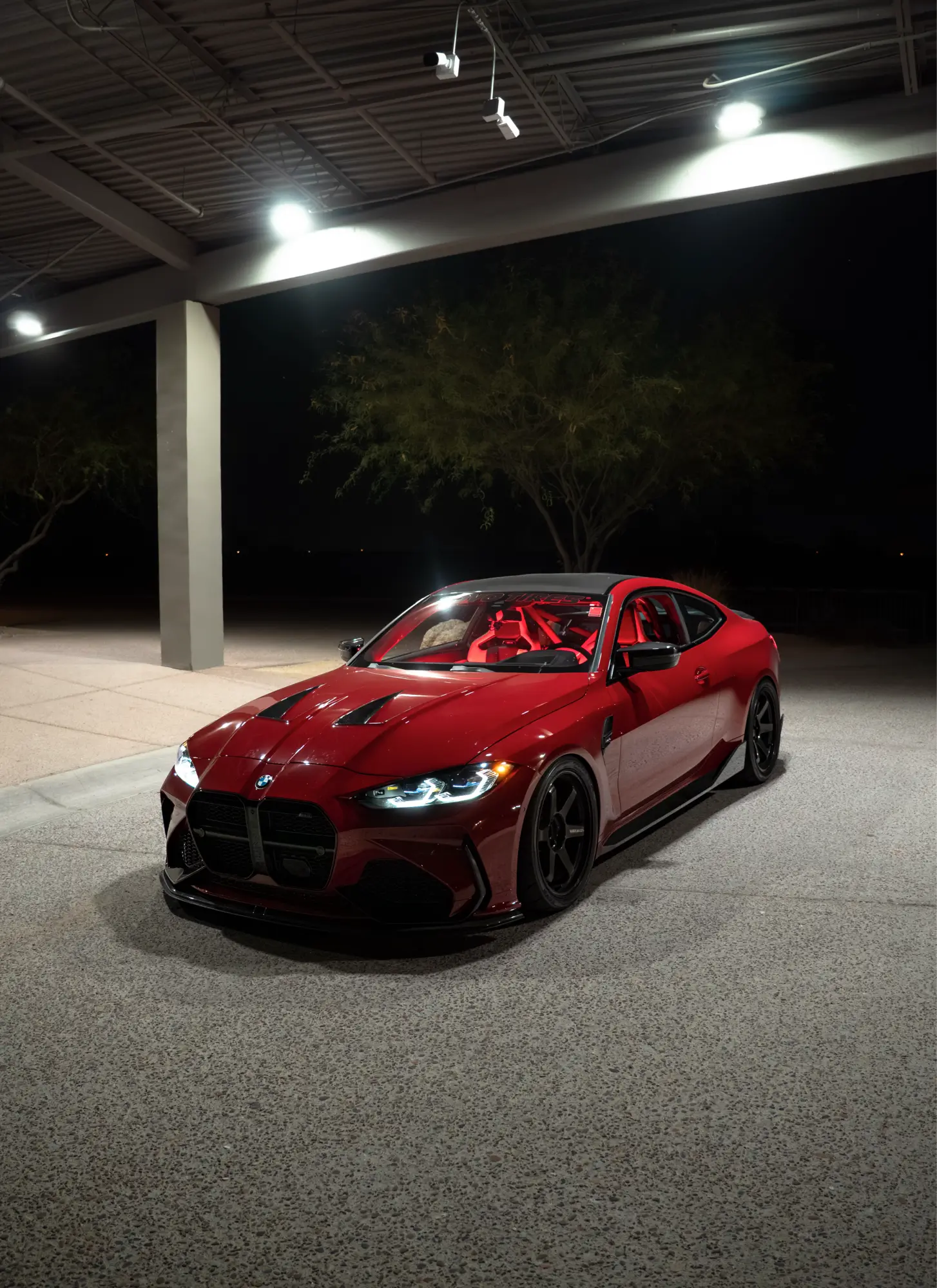 Maroon BMW M4 (G82) shown front three-quarter at night, red interior visible.