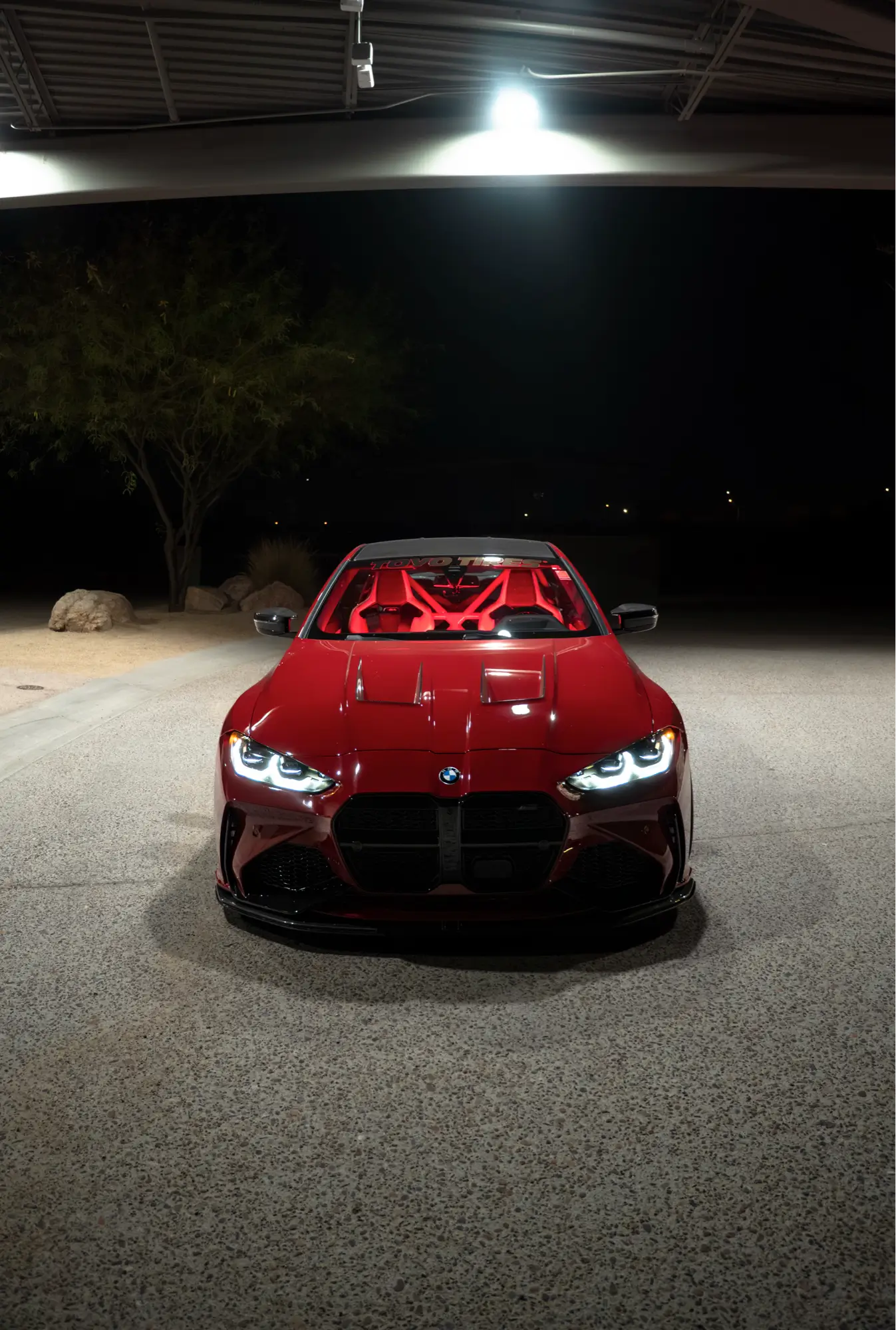 Front view of a maroon BMW M4 (G82) at night on Toyo tires.