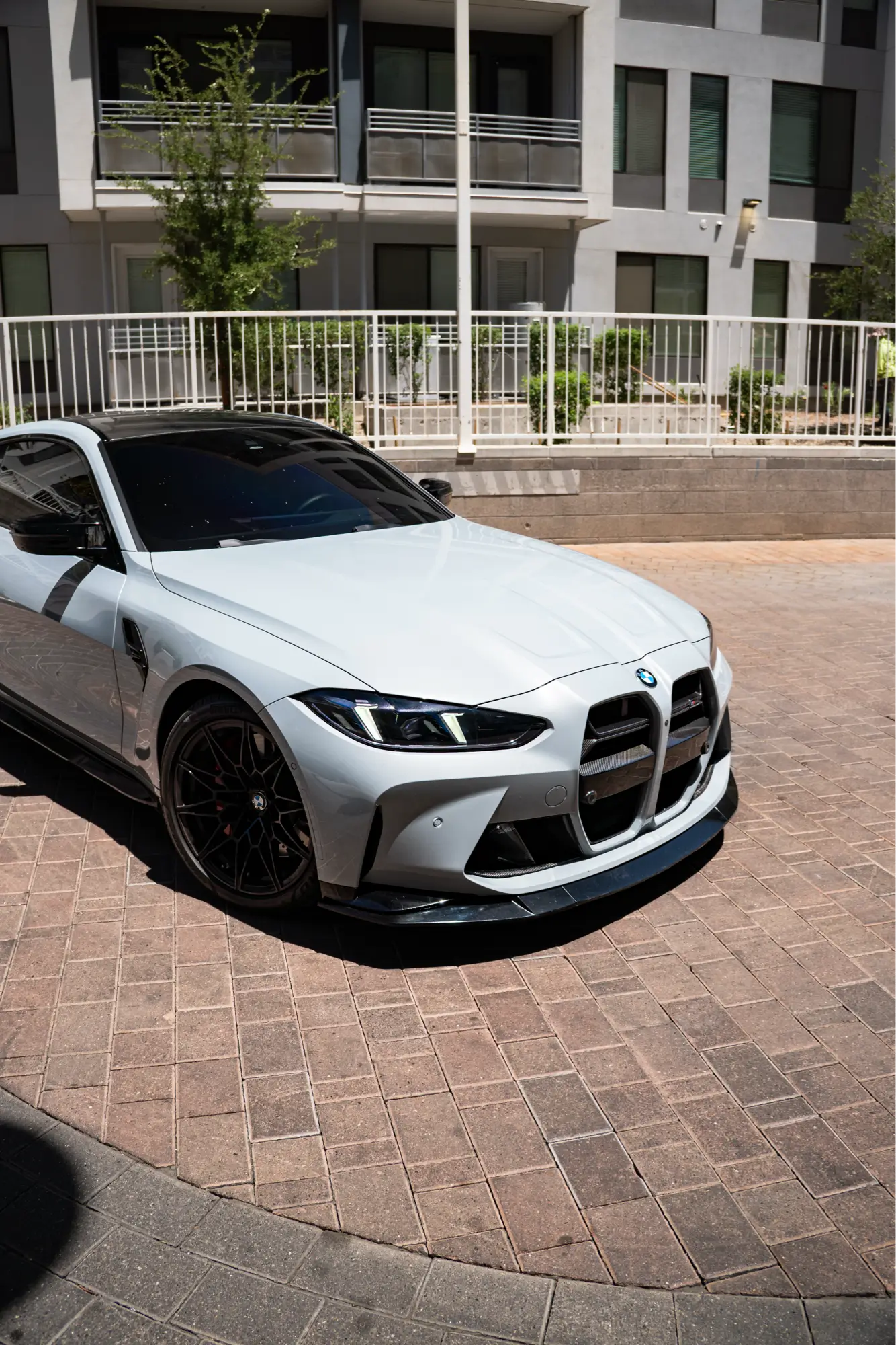 White BMW M4 (G82) shown front three-quarter outside a brick plaza.