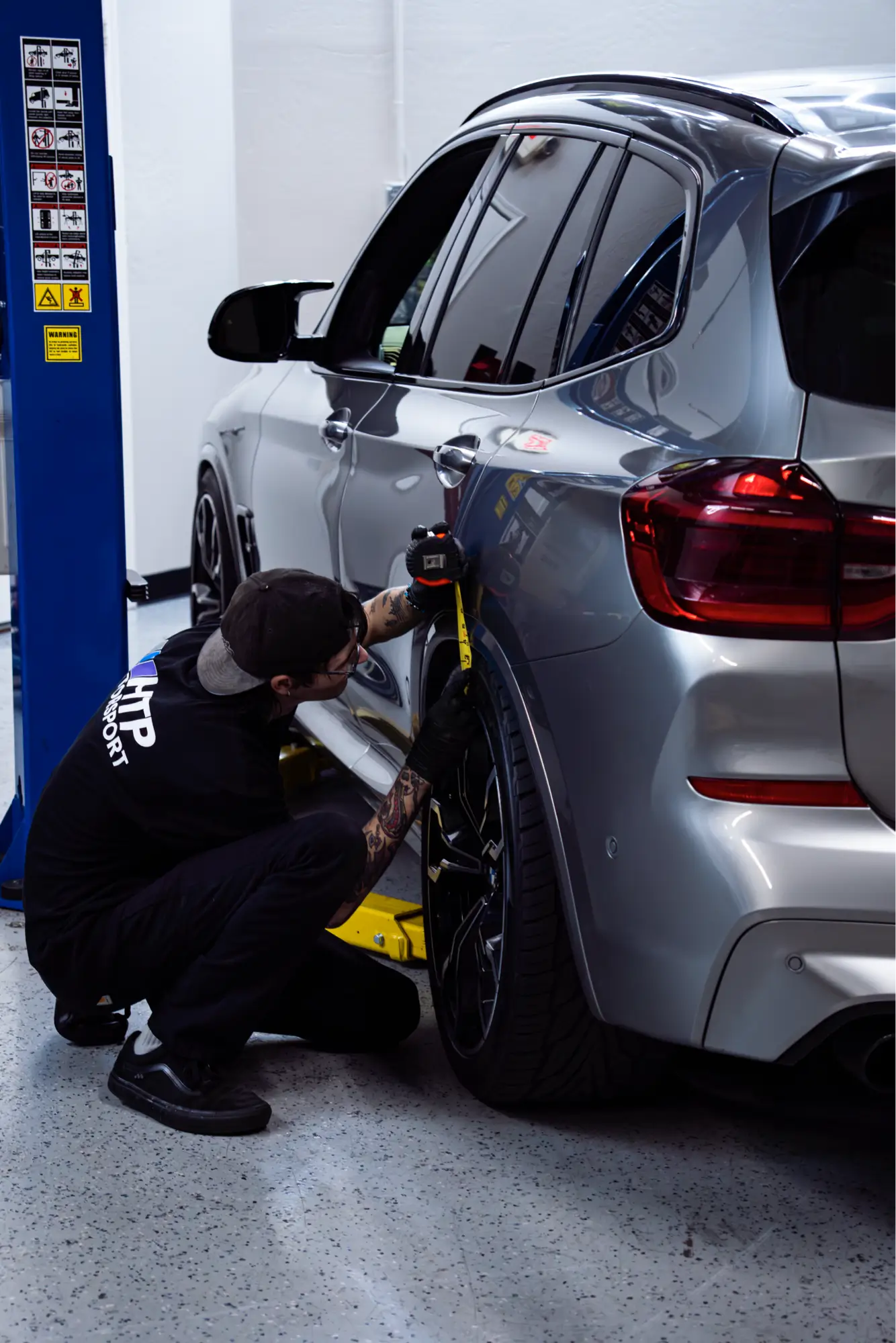 HTP Motorsport mechanic performing a wheel alignment check on a silver BMW X Series SUV.