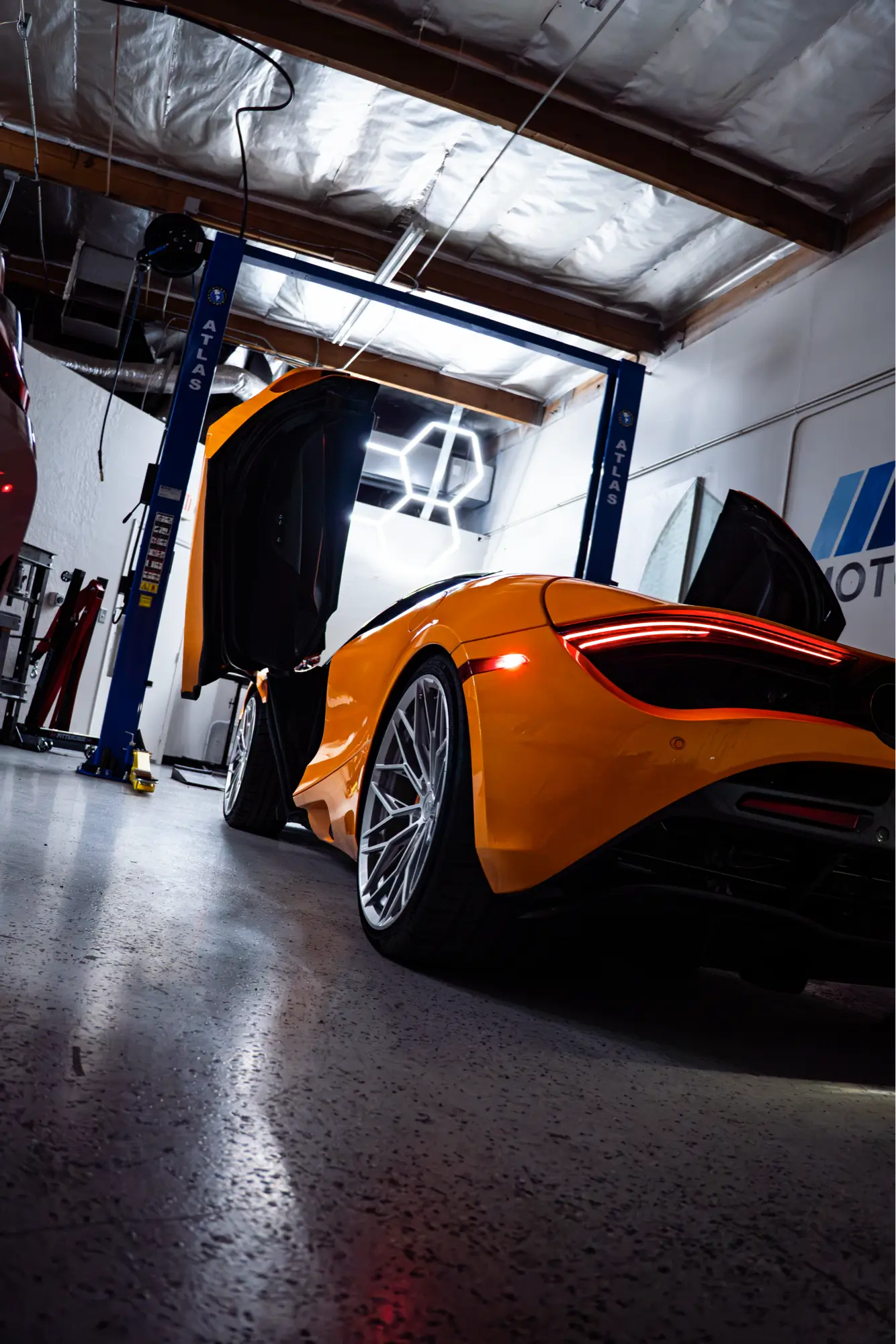 Orange McLaren 720S with its doors raised, shown rear three-quarter on an Atlas lift.