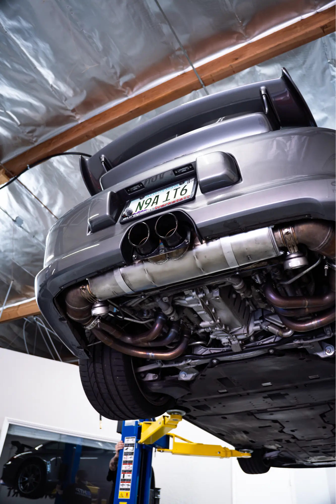 Underside view of a grey Porsche 911 (997) GT3's exhaust on a service lift.