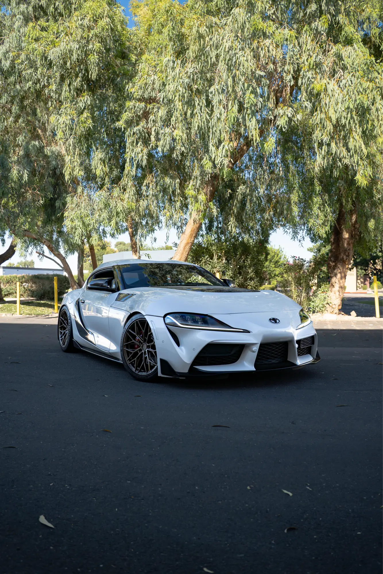 White Toyota Supra (MK5) shown front three-quarter with trees in the background.